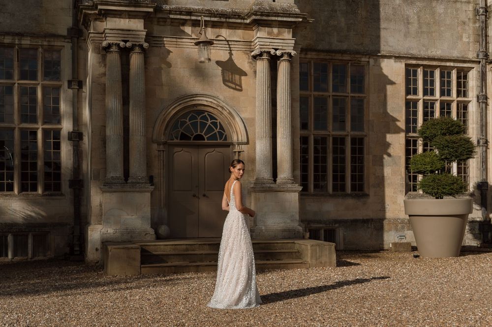 A person in an elegant white gown poses in front of a historic stone building with classical architectural details.