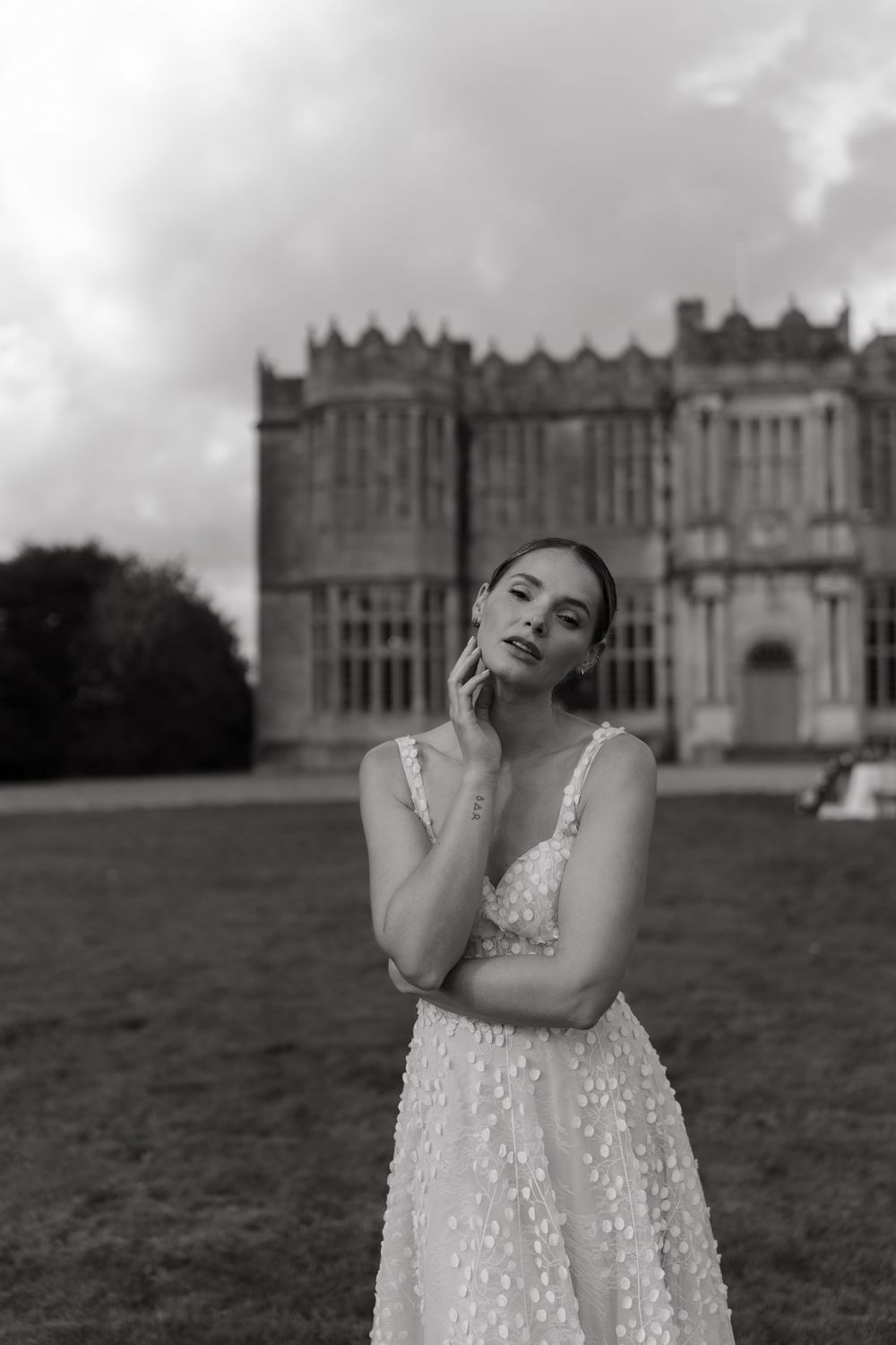 Romantic black and white portrait of someone in a delicate polka dot dress posing in front of a historic Gothic castle.