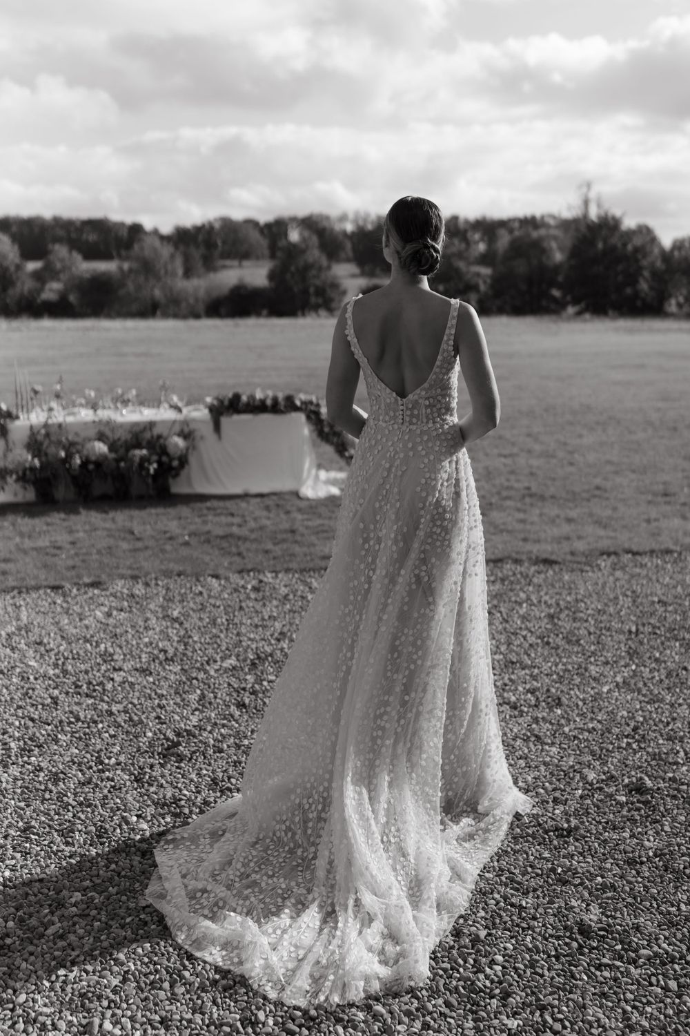 Back view of a bride in a detailed lace wedding dress with open back design standing in a garden setting.