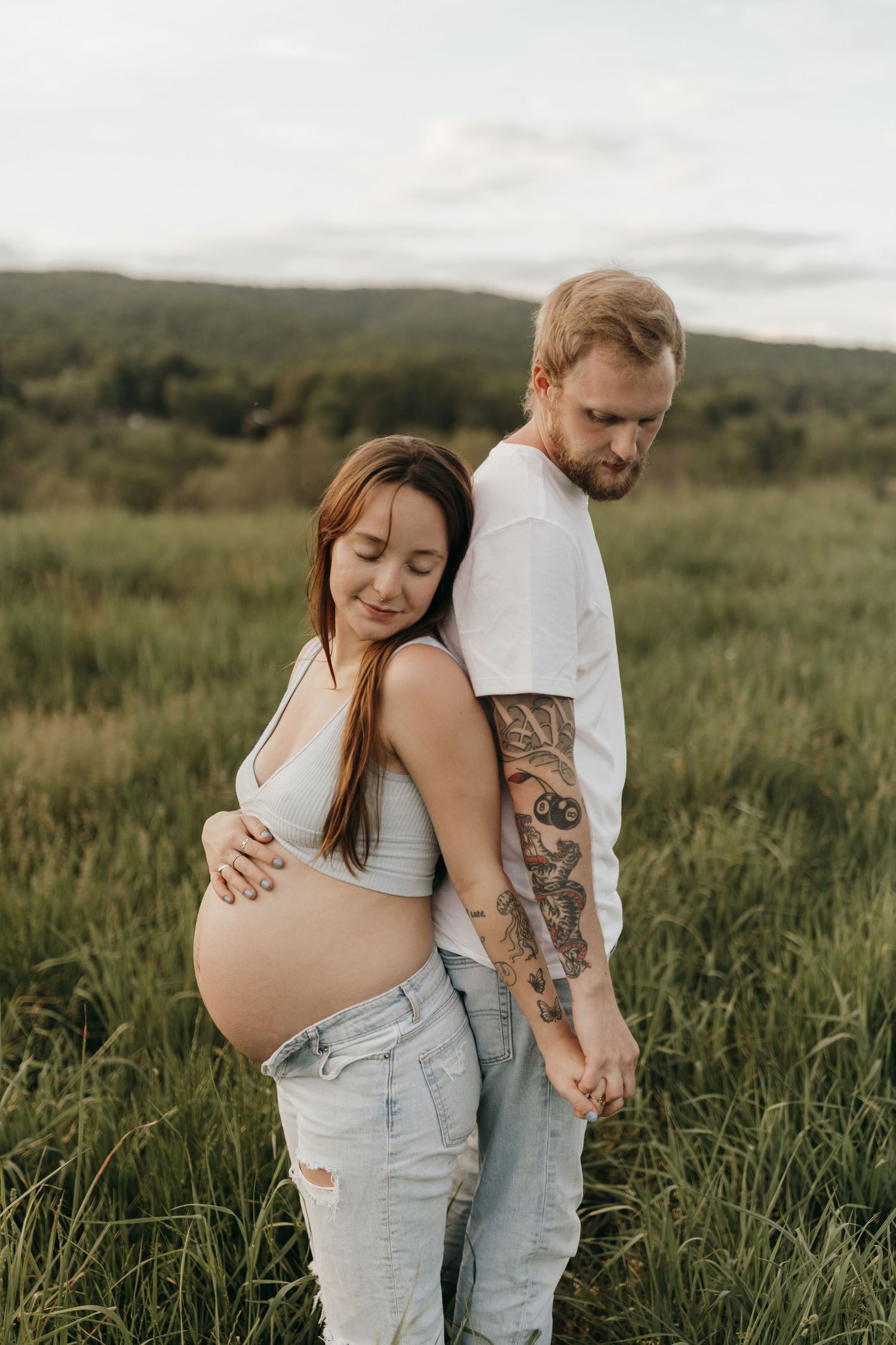Expectant couple stands together in serene meadow during sunset maternity photoshoot.
