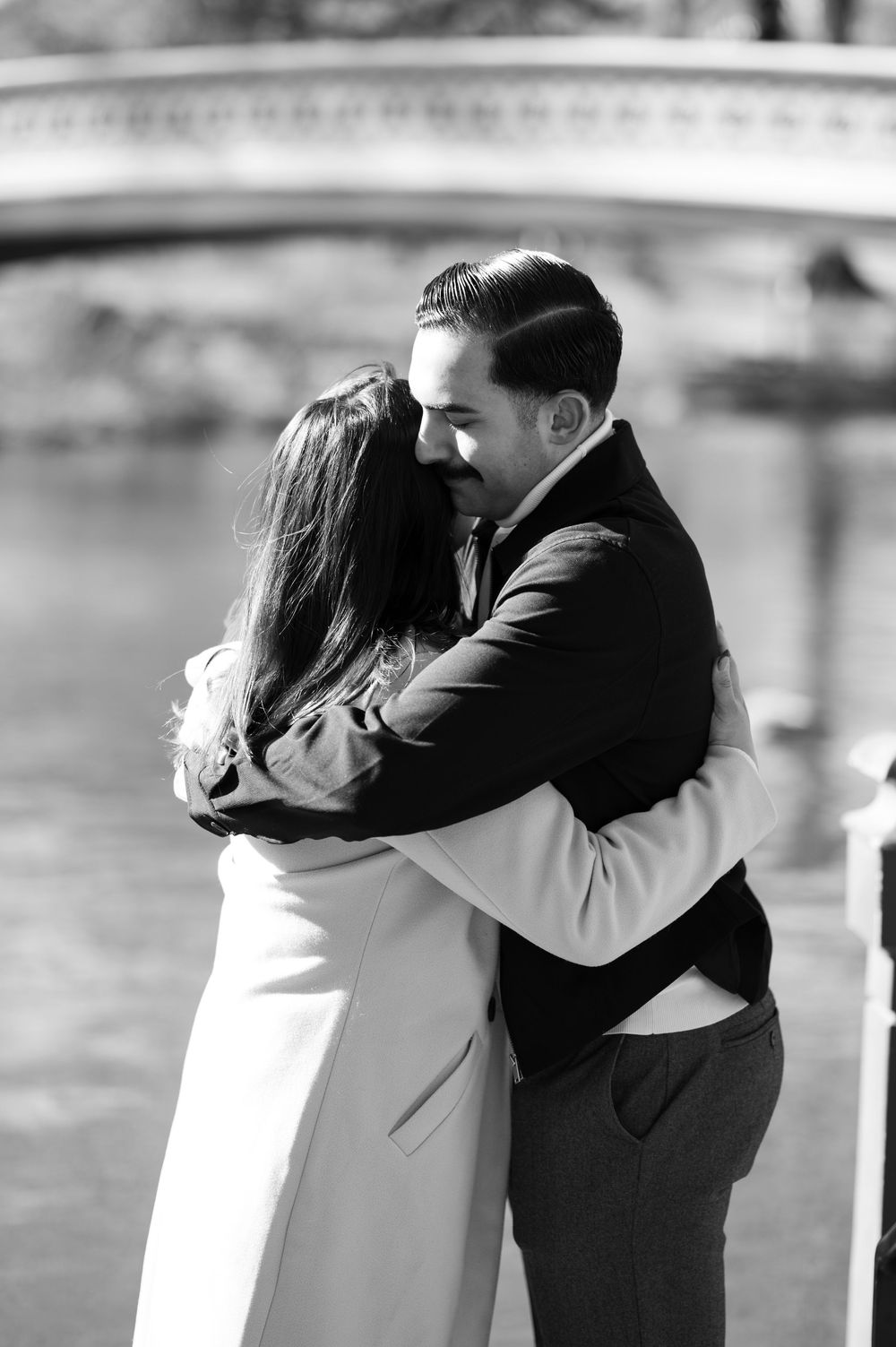 A black and white intimate moment of a couple embracing by a bridge after proposal in Central Park