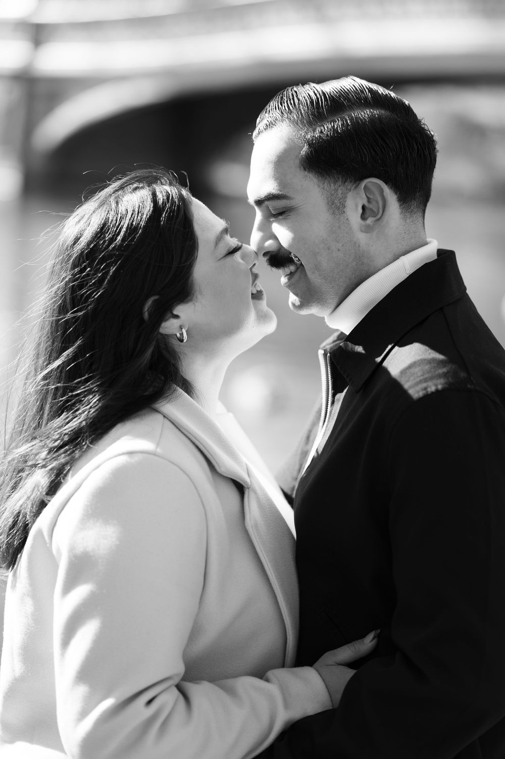 A romantic black and white portrait of a couple about to kiss, in front of Bow Bridge in Central Park