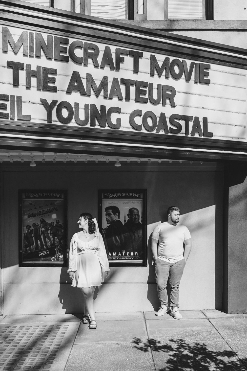 Black and white photo of a movie theater marquee displaying 'Minecraft Movie The Amateur' and 'El Young Coastal'.