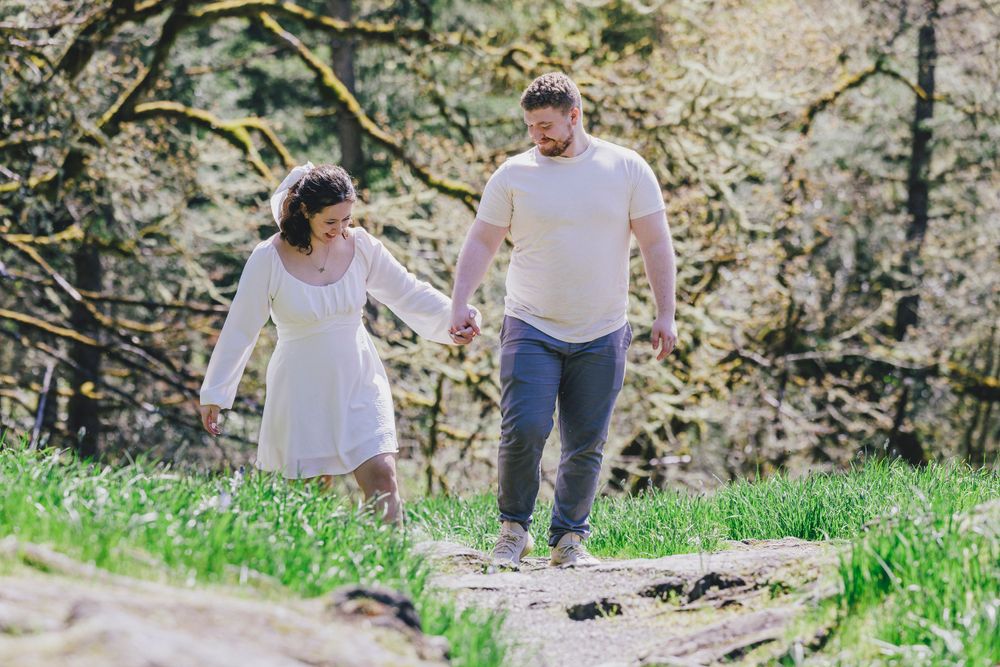 A couple takes a romantic springtime stroll together on a grassy path surrounded by blooming trees.