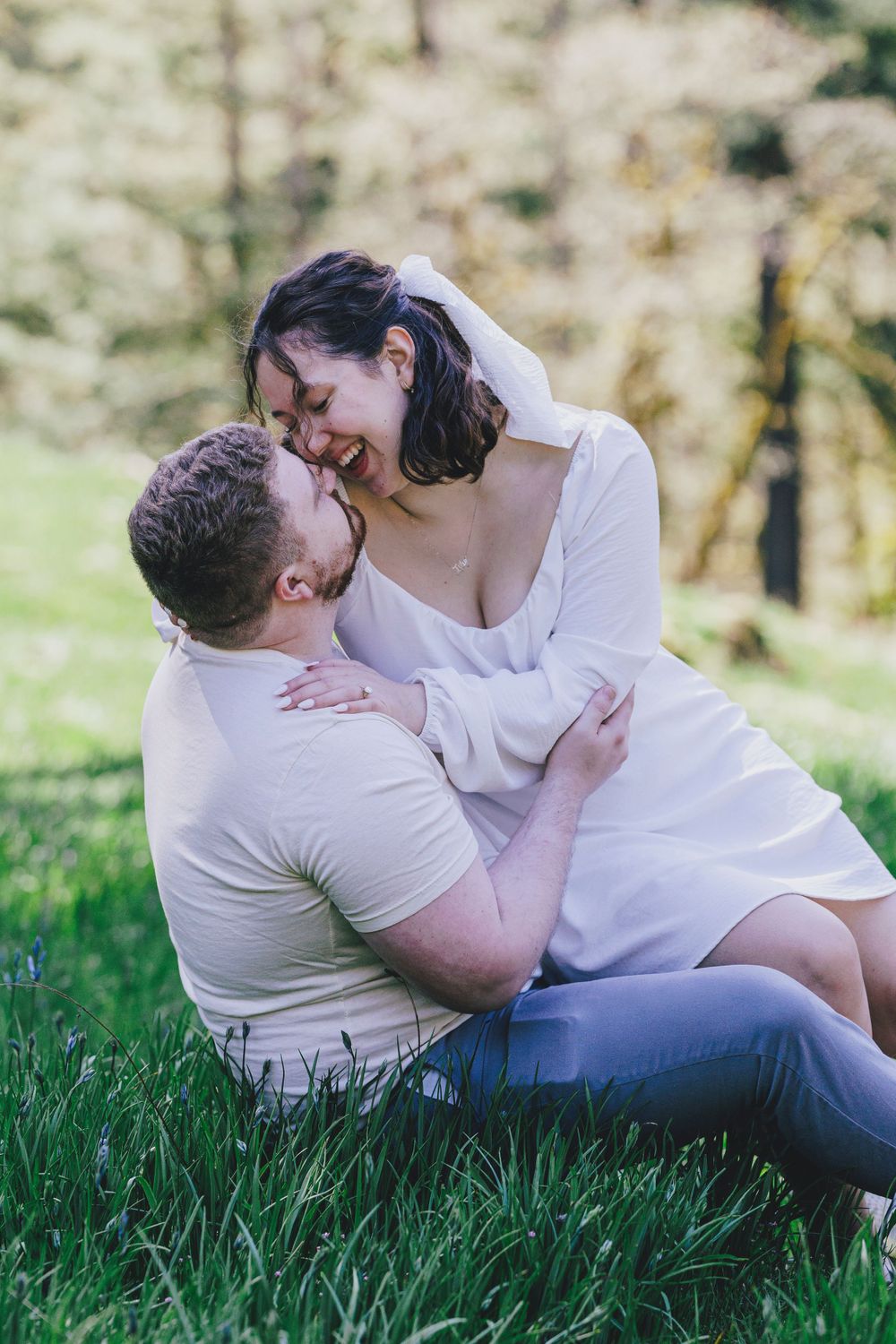 A romantic couple embraces on green grass during an outdoor photo session with soft natural lighting.