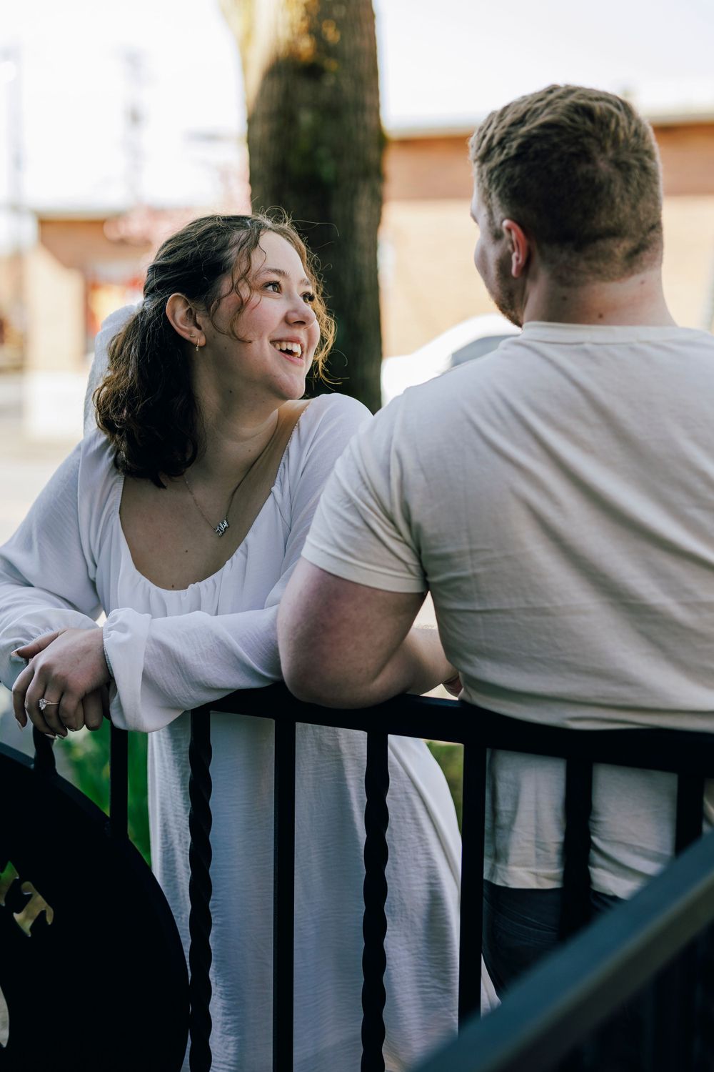 Two people having a casual conversation while leaning on a railing outdoors on a sunny day.