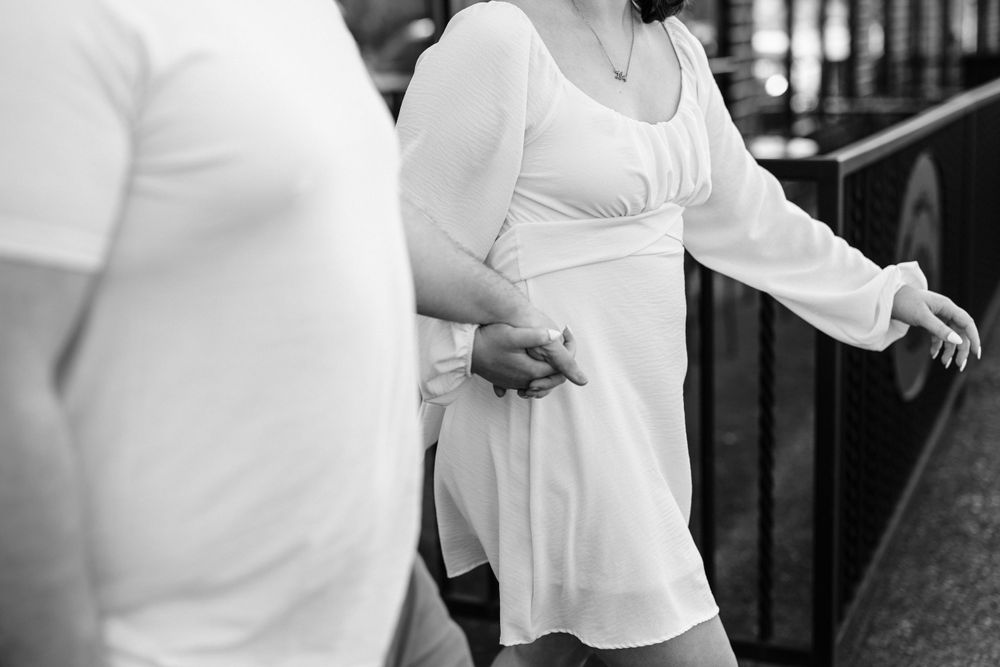 A close-up black and white photo shows someone wearing a white dress being assisted down stairs while holding a railing.
