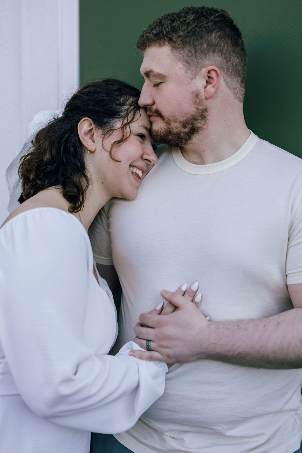 A tender moment between a couple in white clothing against a green background.