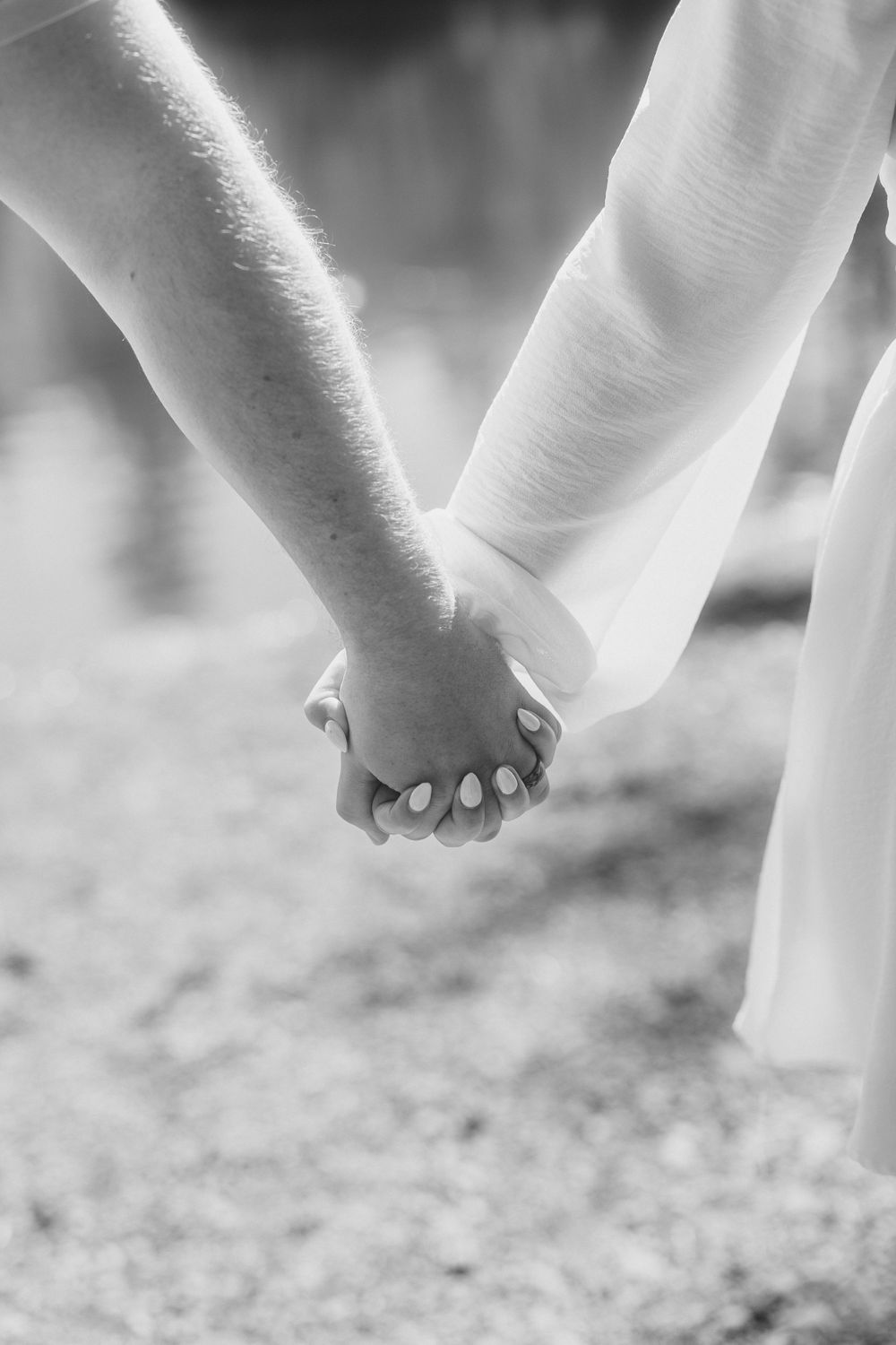 A close-up black and white photo of two hands tenderly holding each other while walking.