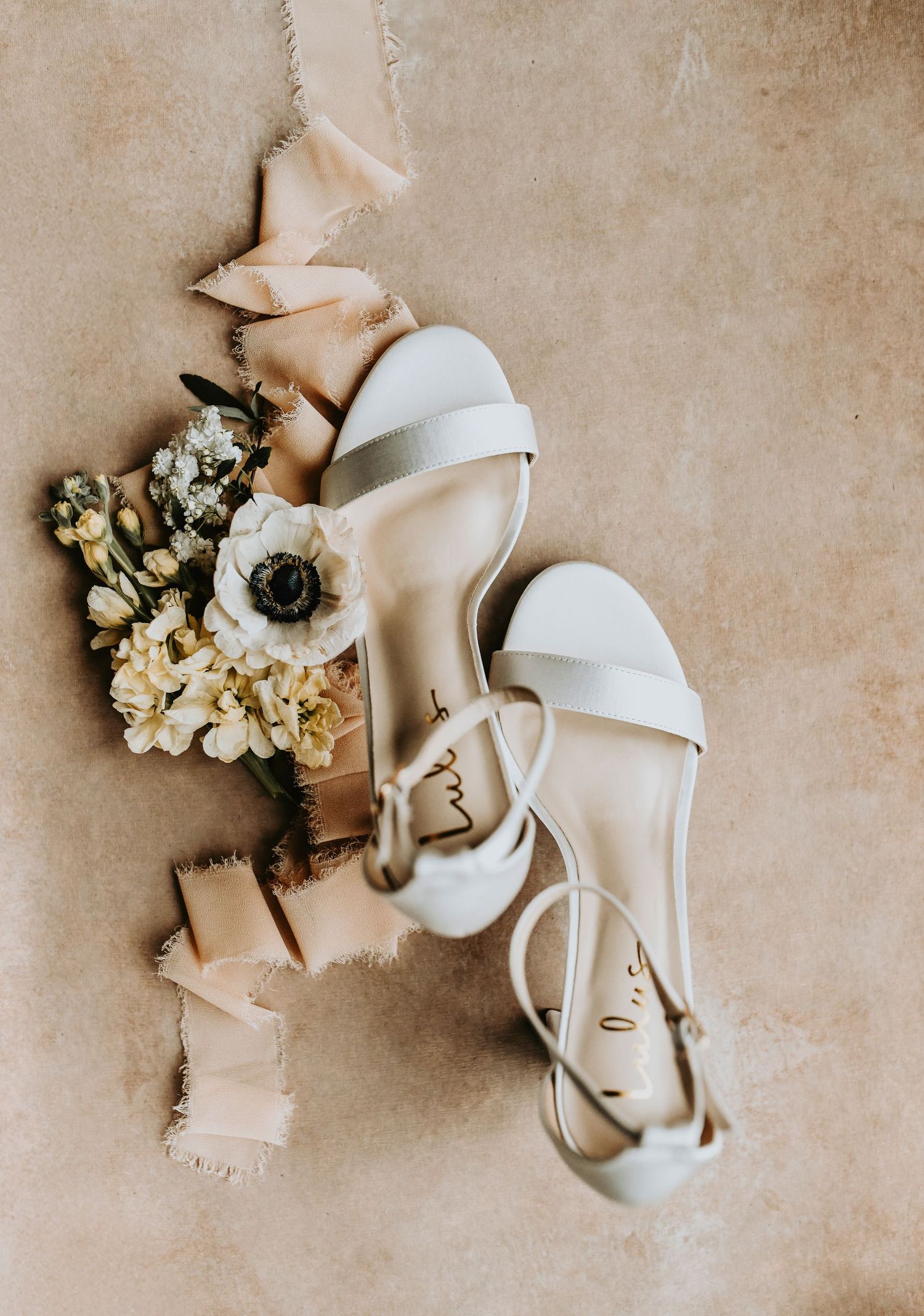 Wedding details flat lay showing bride’s veil, wedding rings, bridal shoes, and a vintage floral tie next to wedding invitation suite.