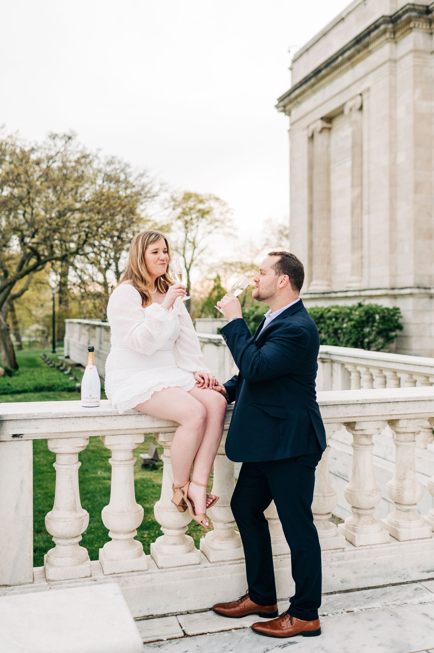 A couple shares a romantic moment on ornate stone balustrade steps outside an elegant classical building in spring.