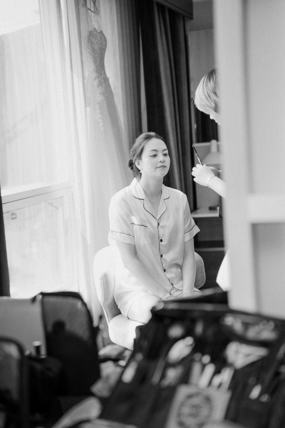 Person in white robe sitting during wedding preparation with dress visible in background.