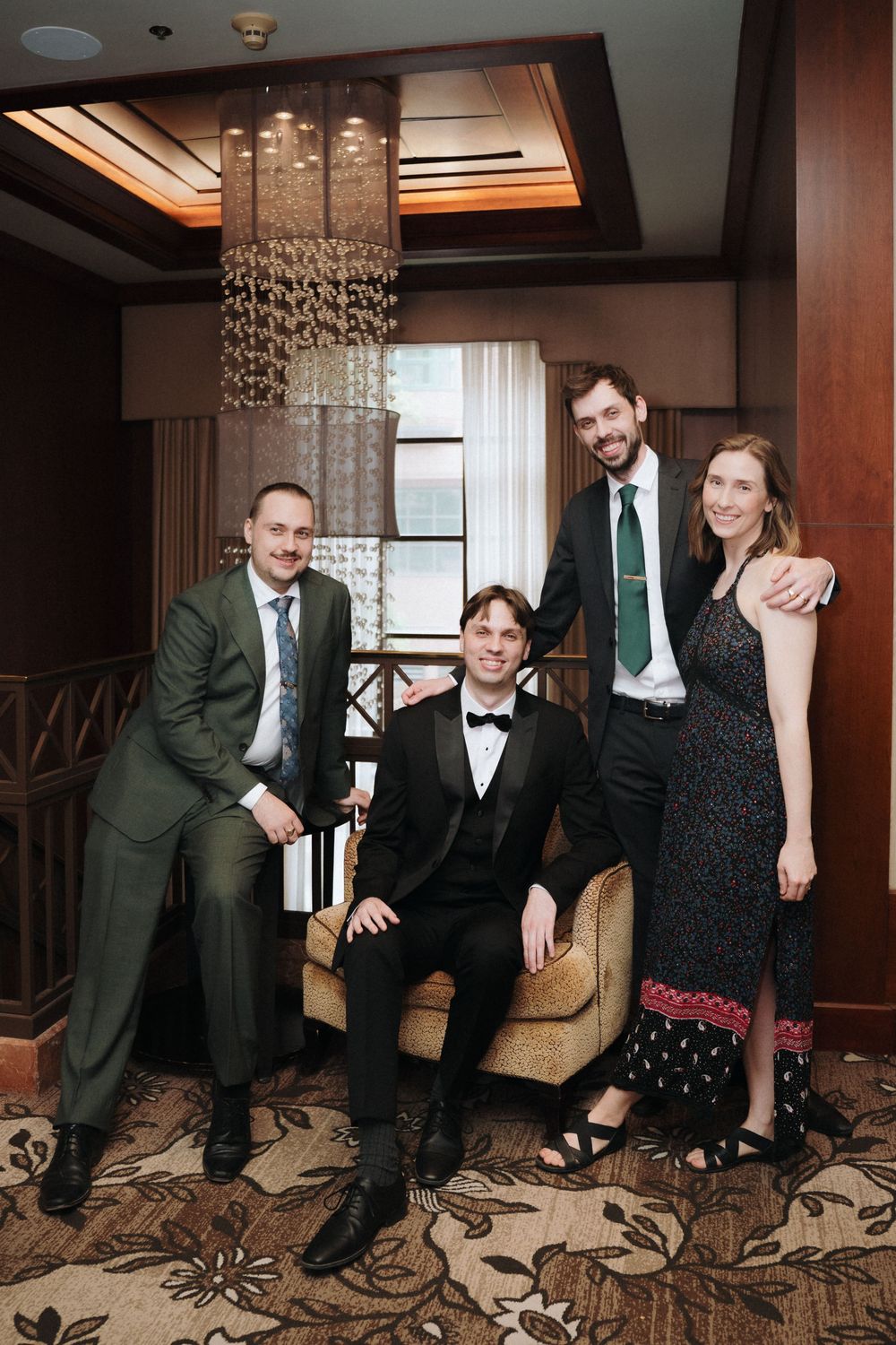 Group photo in elegant room with crystal chandelier and floral carpet.