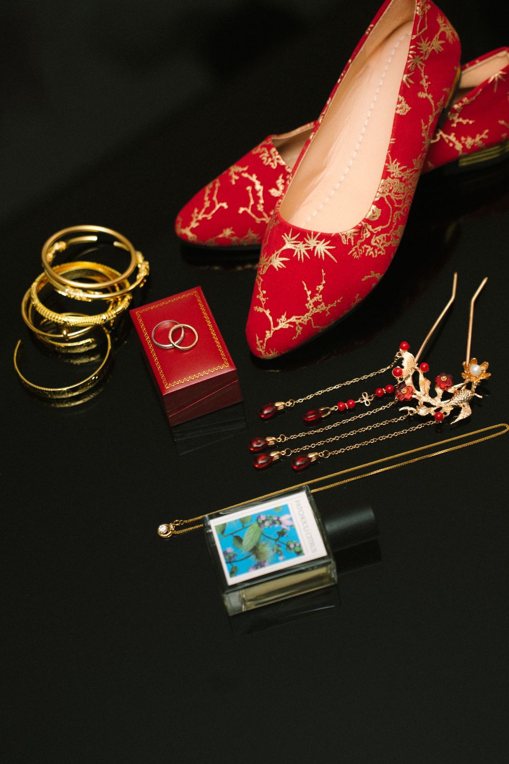 Wedding accessories including red embroidered flats, gold bangles, and jewelry box on black surface.