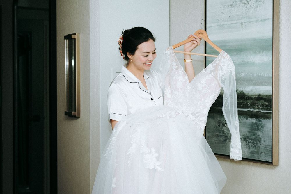 A white lace wedding dress being held up in a bridal preparation room.