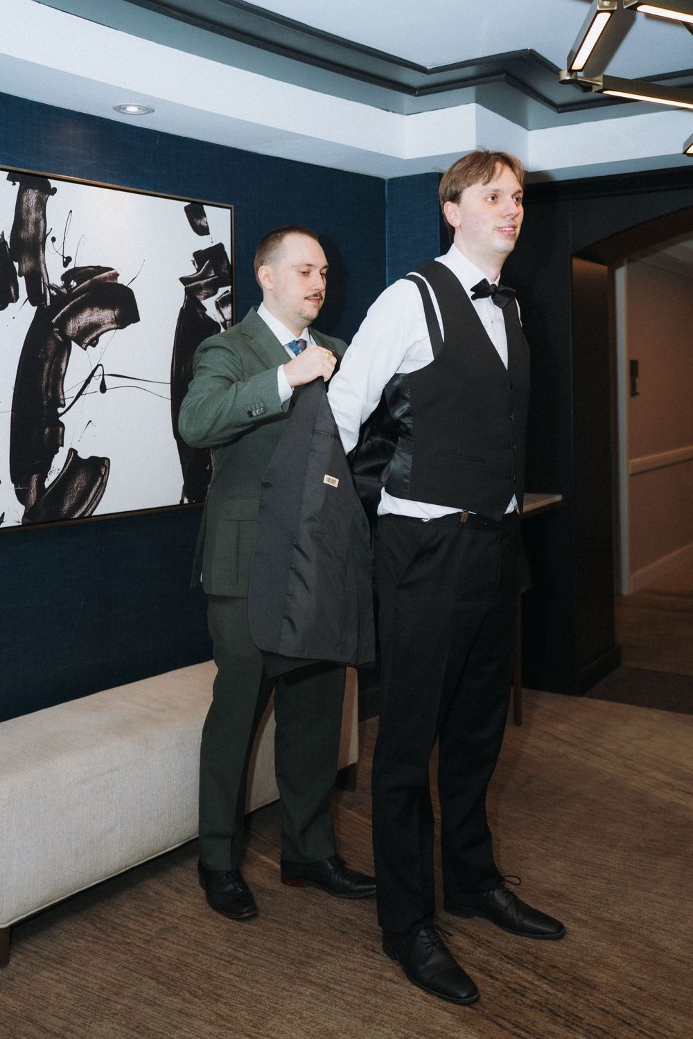 Two people in formal attire standing in front of abstract wall art.