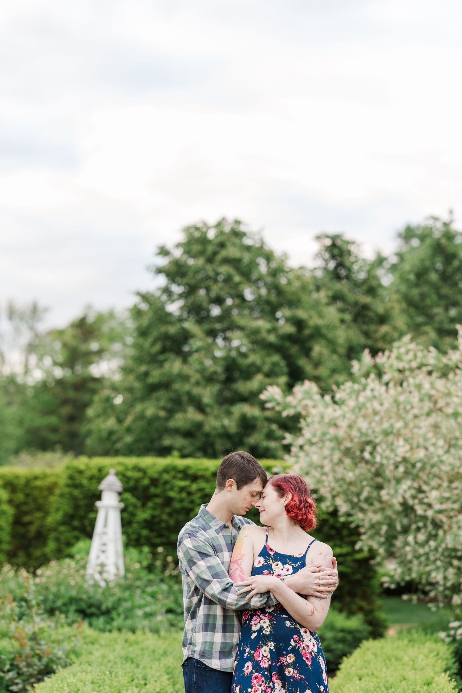 A romantic moment between two people embracing in a lush garden with blooming trees and a decorative obelisk at Cantigny Park