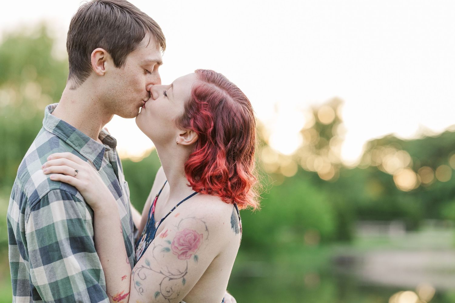 A couple shares a tender kiss outdoors during golden hour surrounded by greenery and natural light at Cantigny Park