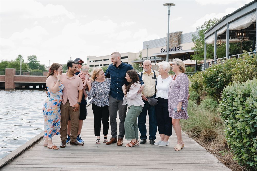 Group of people enjoying a casual gathering on a wooden boardwalk by the waterfront near a modern building.