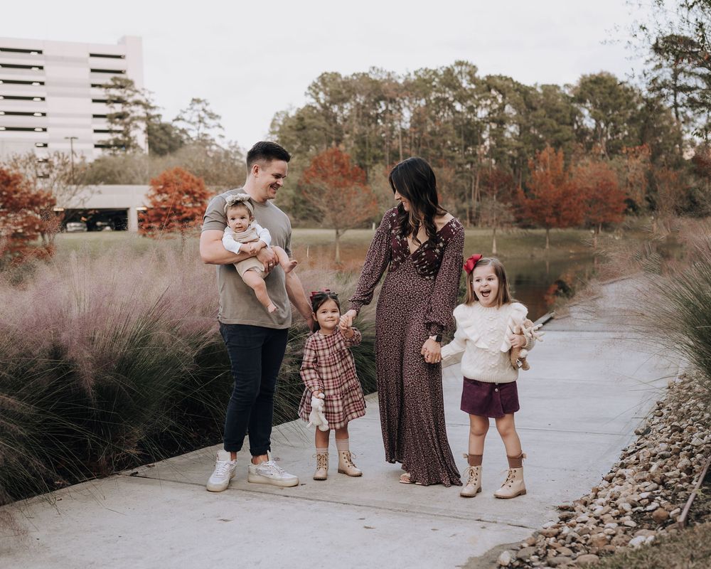 Family standing together on a path surrounded by autumn grasses and fall foliage near a modern building.