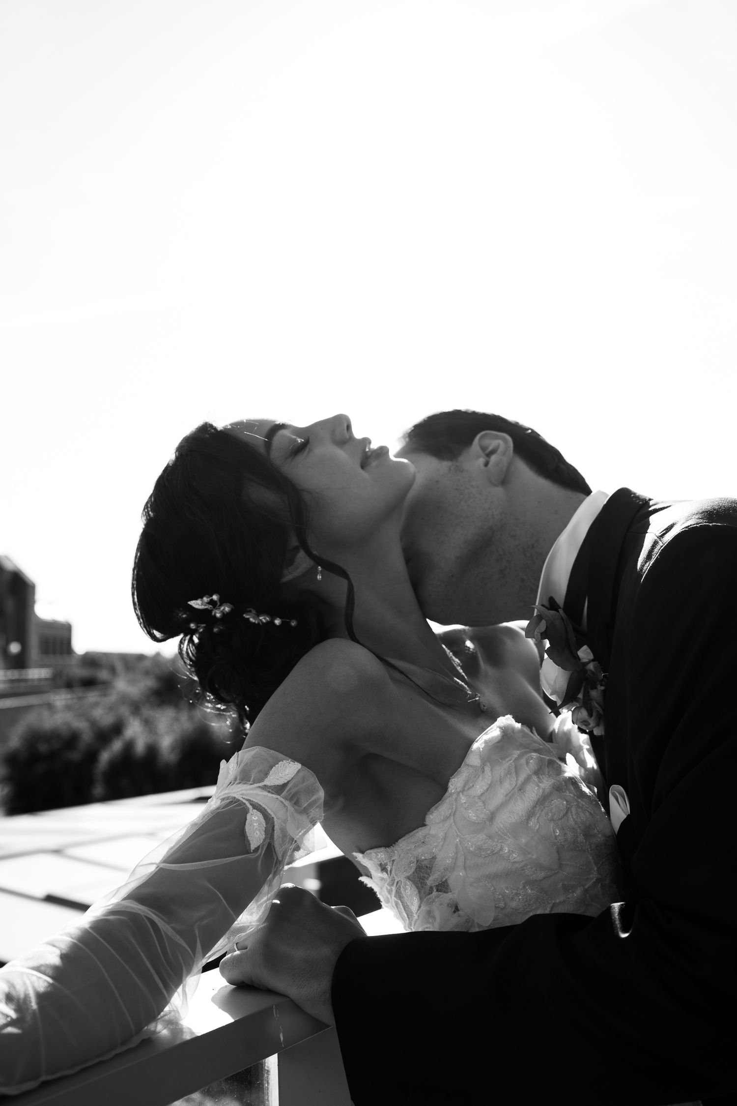 Black and white romantic portrait of a couple sharing an intimate moment, dancing on a balcony in dramatic backlit lighting.