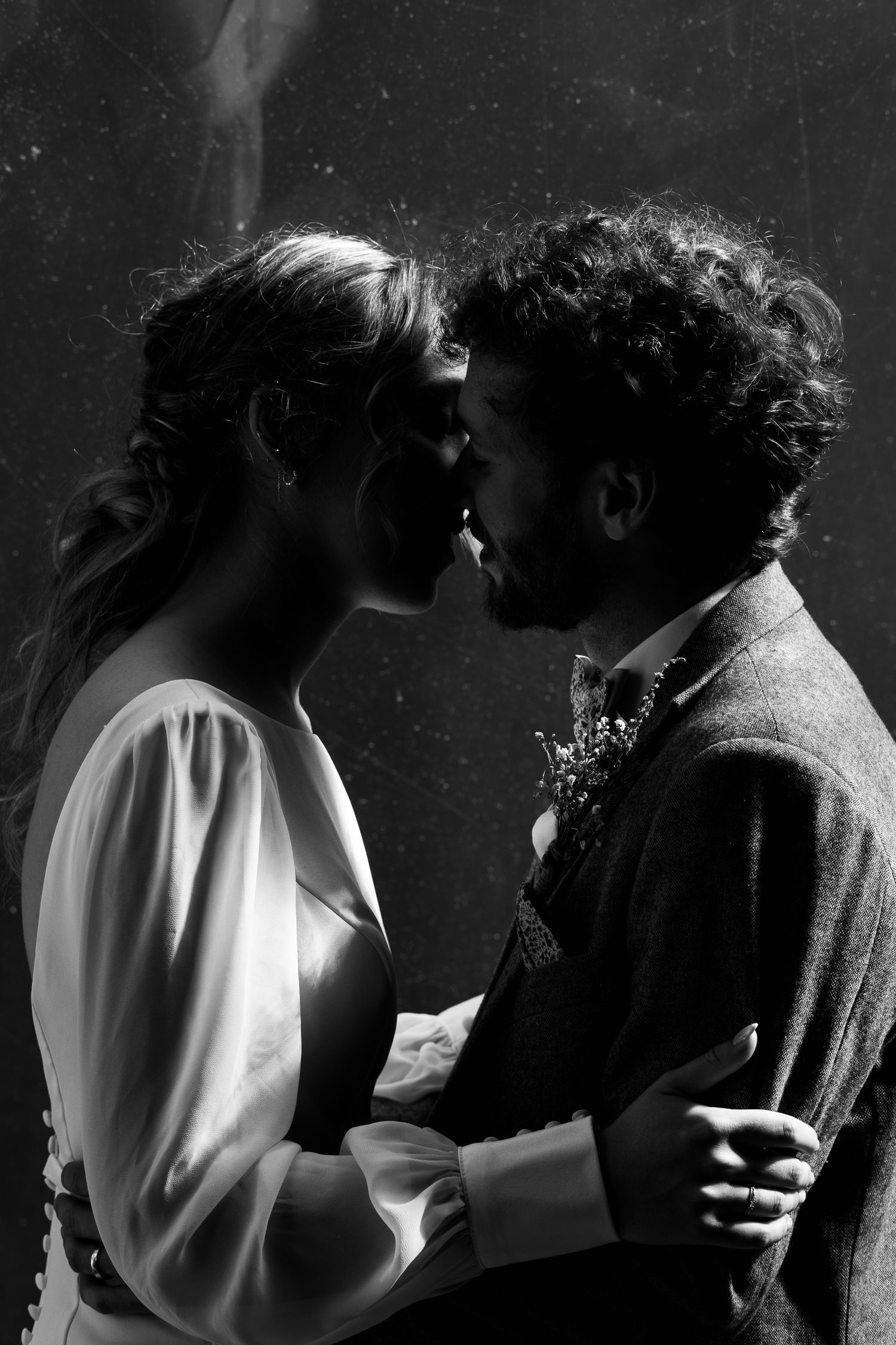 A black and white romantic portrait of an intimate moment between a couple in wedding attire with dramatic lighting.