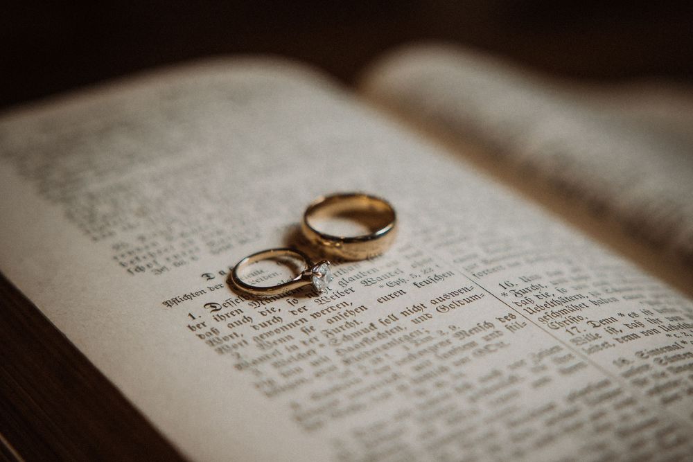 Two wedding rings resting on an open book with text visible beneath them in soft lighting.