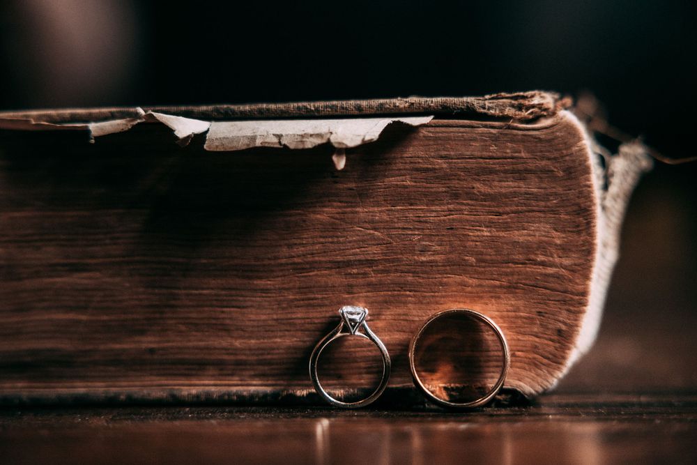 Two gold wedding rings displayed on dark wooden surface with rustic texture and dramatic lighting.