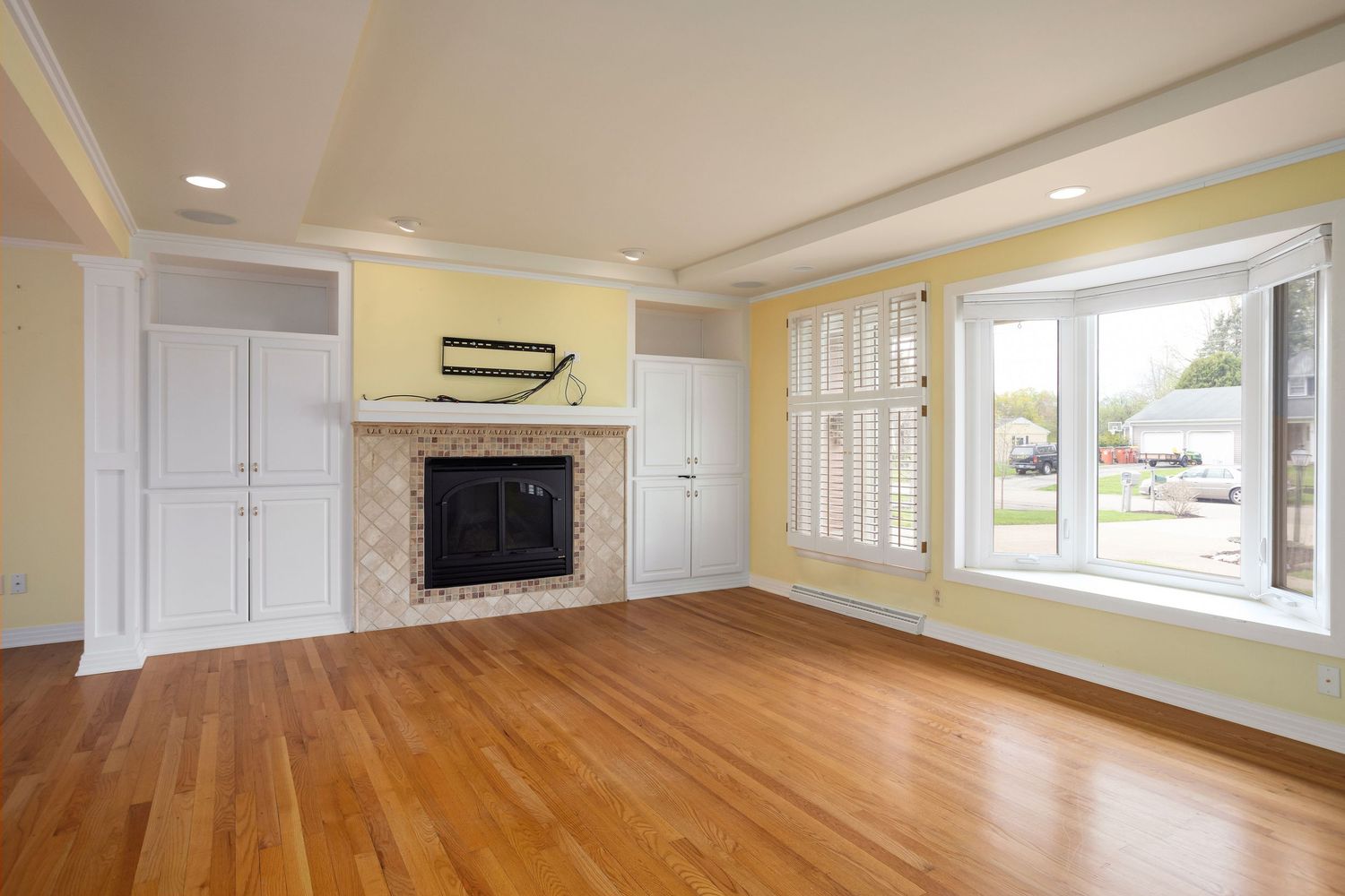 Living room with hardwood floors, built-in fireplace, yellow walls, and large bay windows.