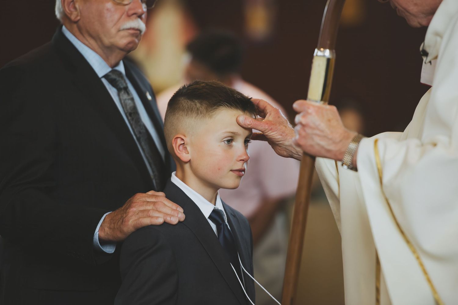 A young boy in a dark suit receives a religious blessing during a formal ceremony.