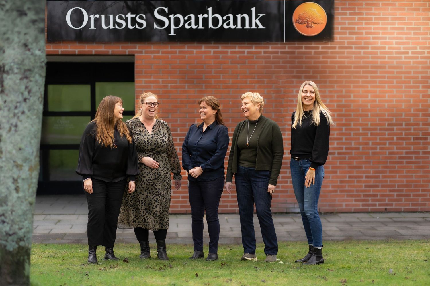 A group of staff members stand outside a brick building with the Orusts Sparbank sign visible.