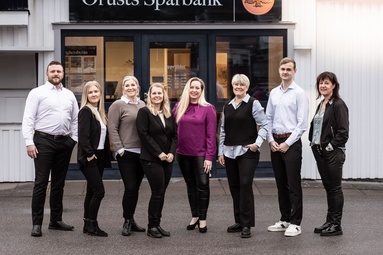 A professional team of people standing in front of a bank location wearing business attire.