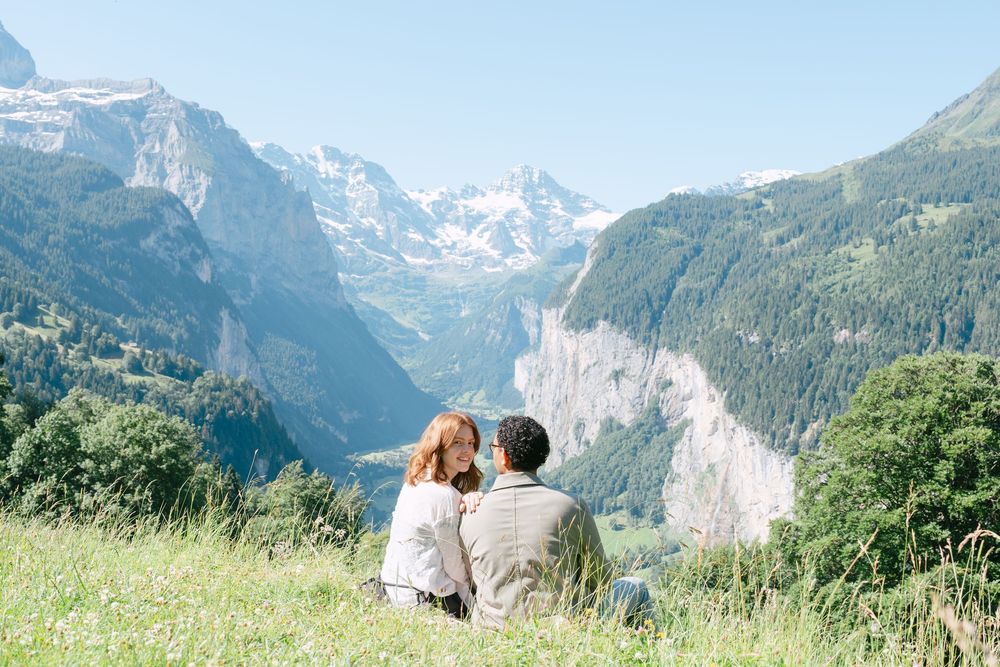 A couple sits together on a grassy meadow overlooking the stunning Swiss Alps and Lauterbrunnen Valley in Switzerland.