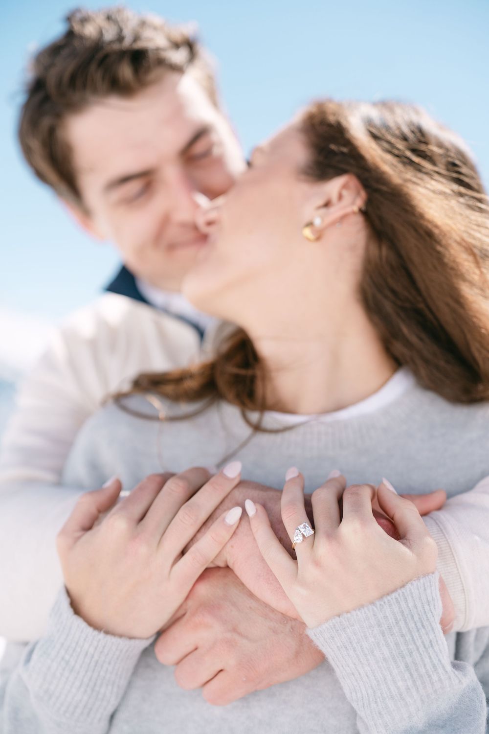 Intimate couple in light sweaters embrace and share a tender moment against a bright background.