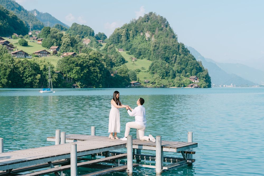 A couple sharing a romantic proposal moment on a wooden dock overlooking a serene mountain lake in Switzerland.