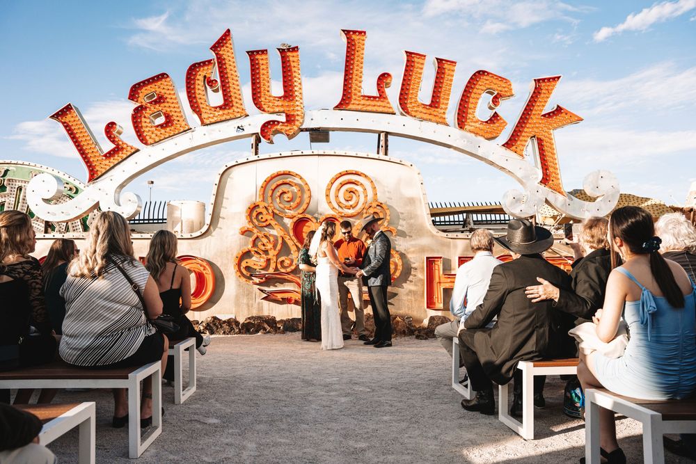 Many patrons gather under a colorful vintage Lady Luck sign at a vibrant carnival or fairground setting.