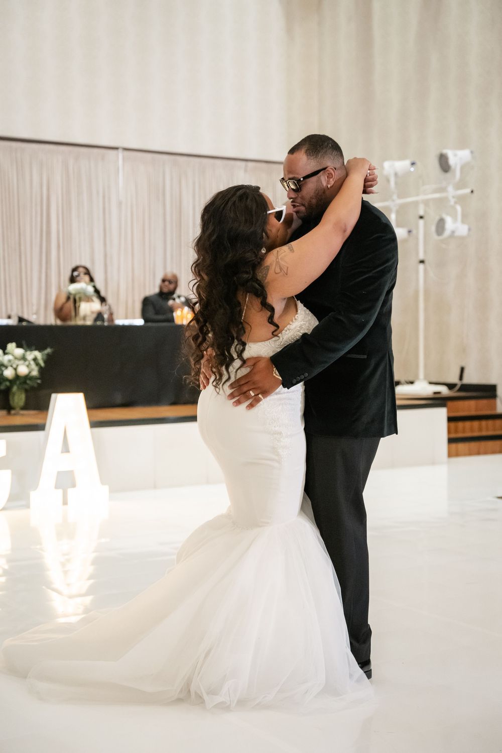 Newlyweds share their first dance at a wedding reception in a modern white venue with dramatic lighting.