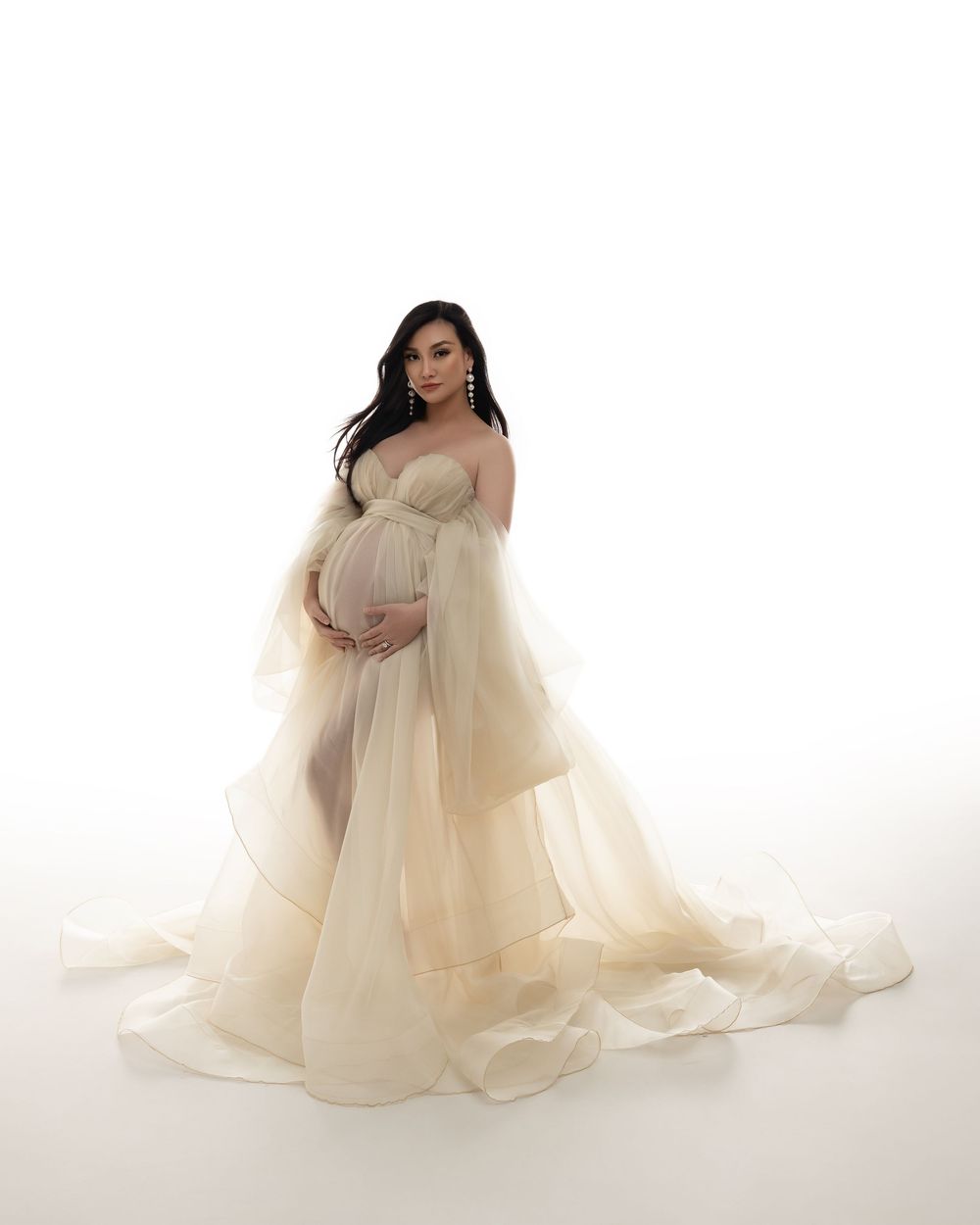 A flowing cream-colored sheer maternity gown is showcased in four elegant poses against a white backdrop.