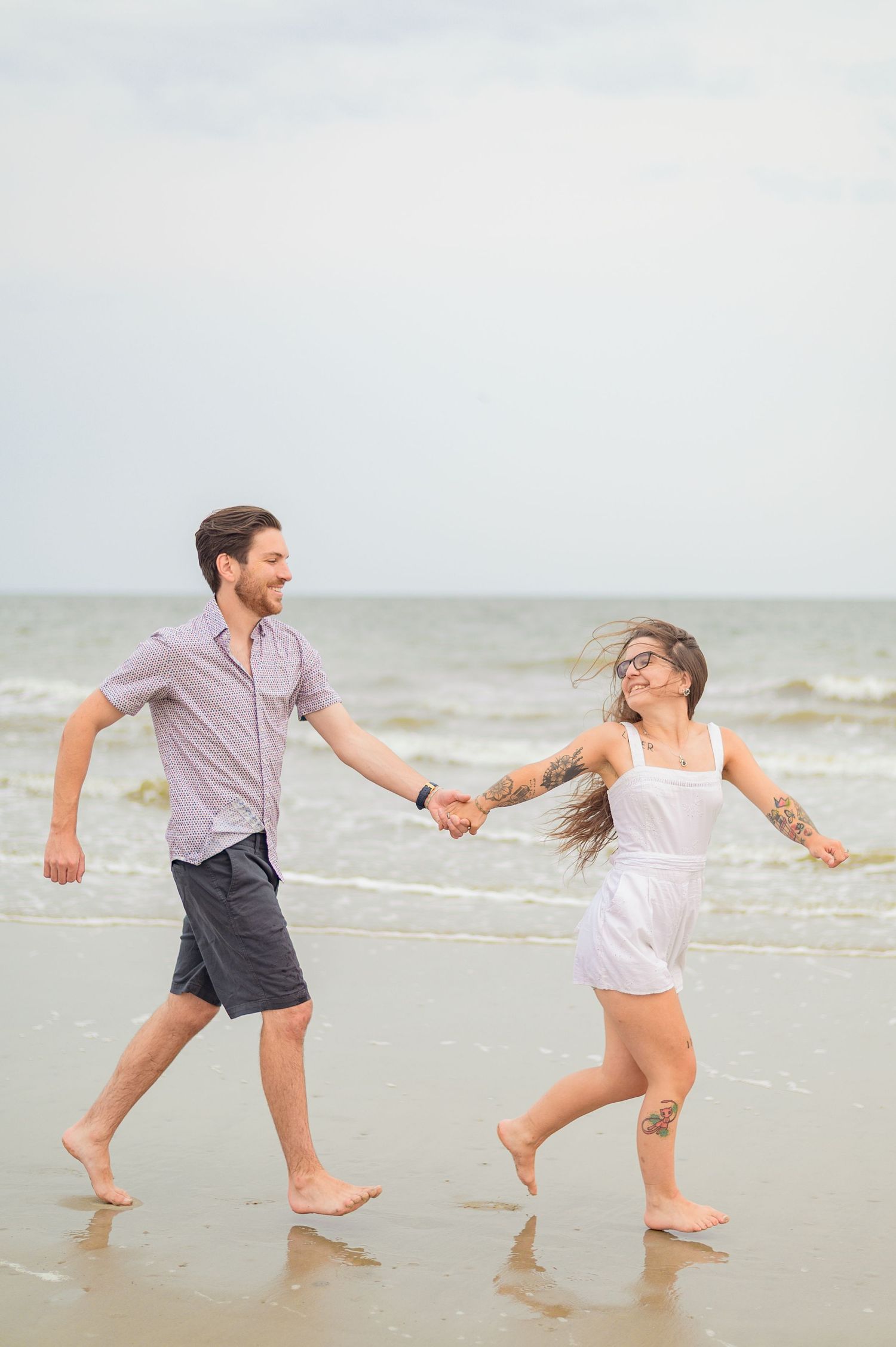 Playful couple splashes and dances in shallow ocean waves at the beach.