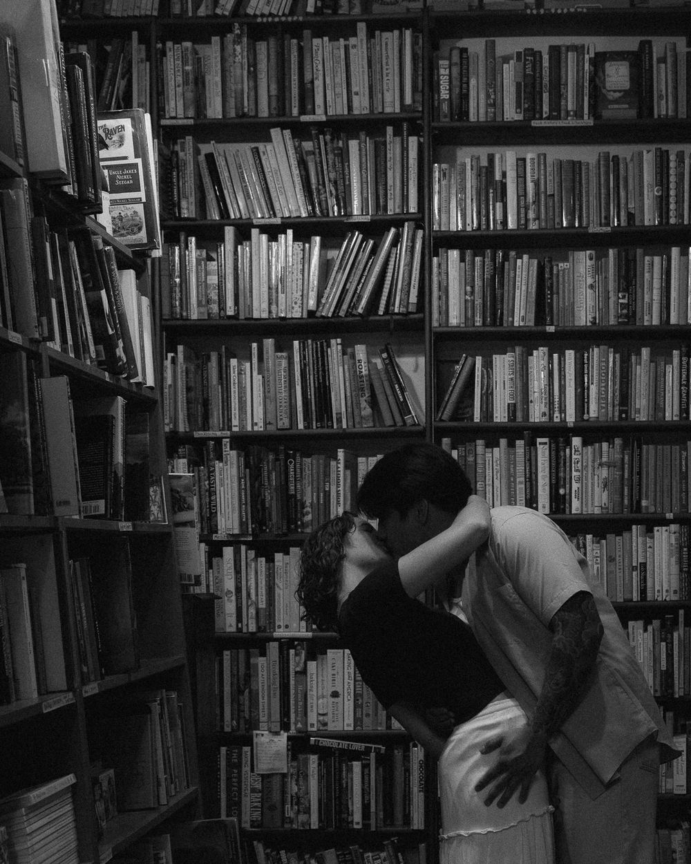 A couple kissing in an aisle full of books.