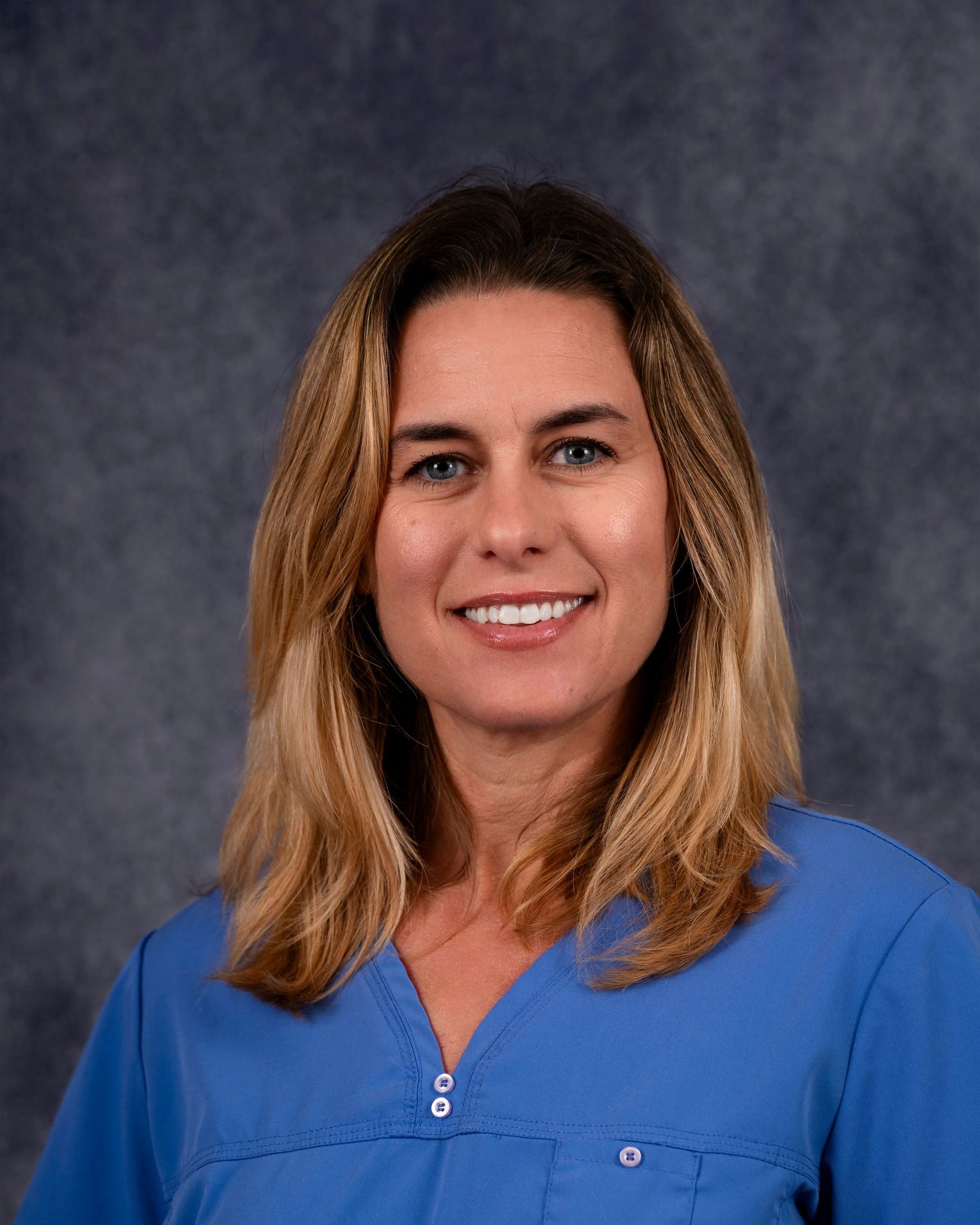 Professional headshot photo on gray background showing blonde hair, white teeth, and bright blue medical scrubs.