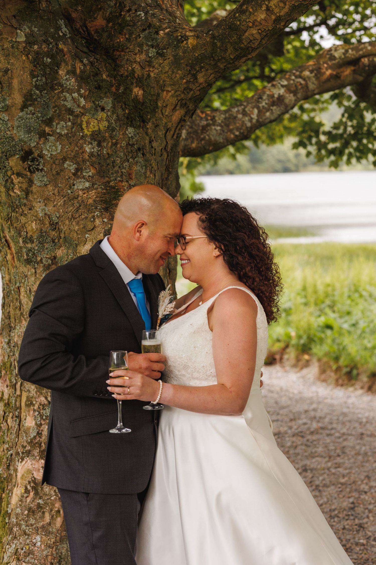 Romantic newlyweds share an intimate moment together under a large tree during outdoor wedding photos.