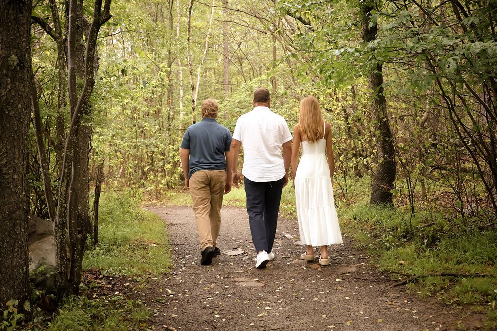 People walking on a tree-lined dirt path through lush green woods during spring or summer.