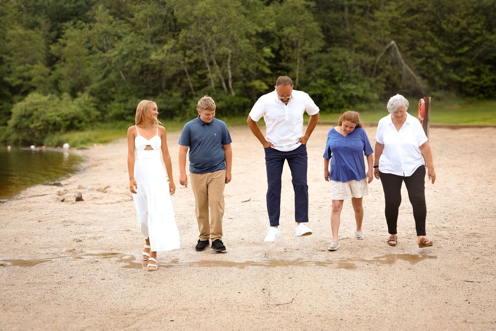 A group of people walking and laughing together on a sandy beach near a wooded shoreline.