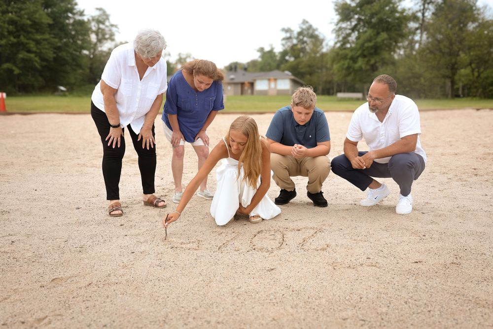 A group sits together on a sandy beach wearing casual white and navy blue clothing during a photo session.