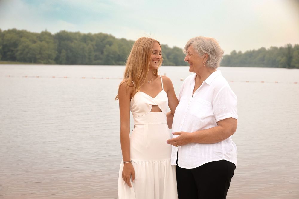 Two people in light colored clothing share romantic moments by a serene lakeside at sunset.