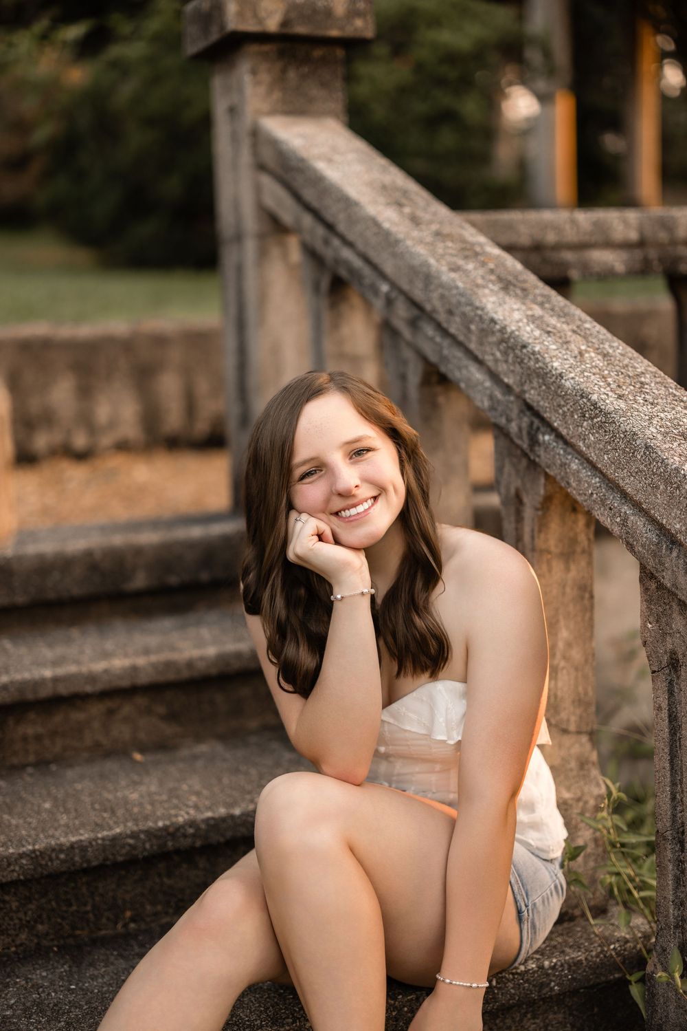 Person sitting on concrete steps outdoors at sunset wearing a white top.