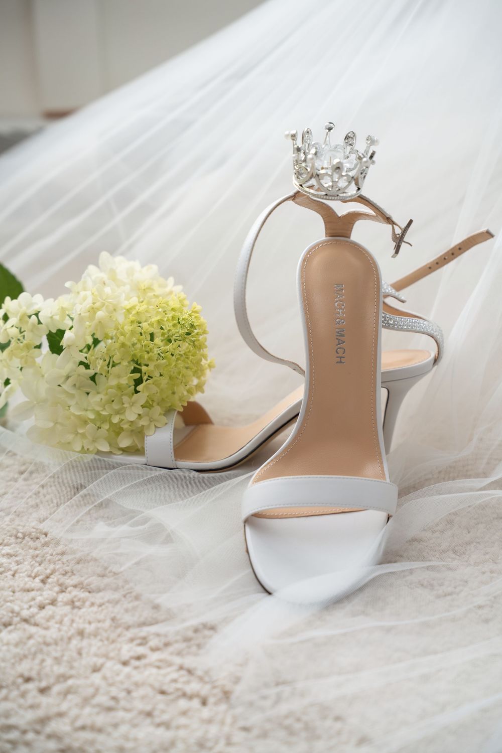 White bridal shoes and delicate hydrangea flowers arranged on flowing tulle fabric create an elegant wedding detail composition.