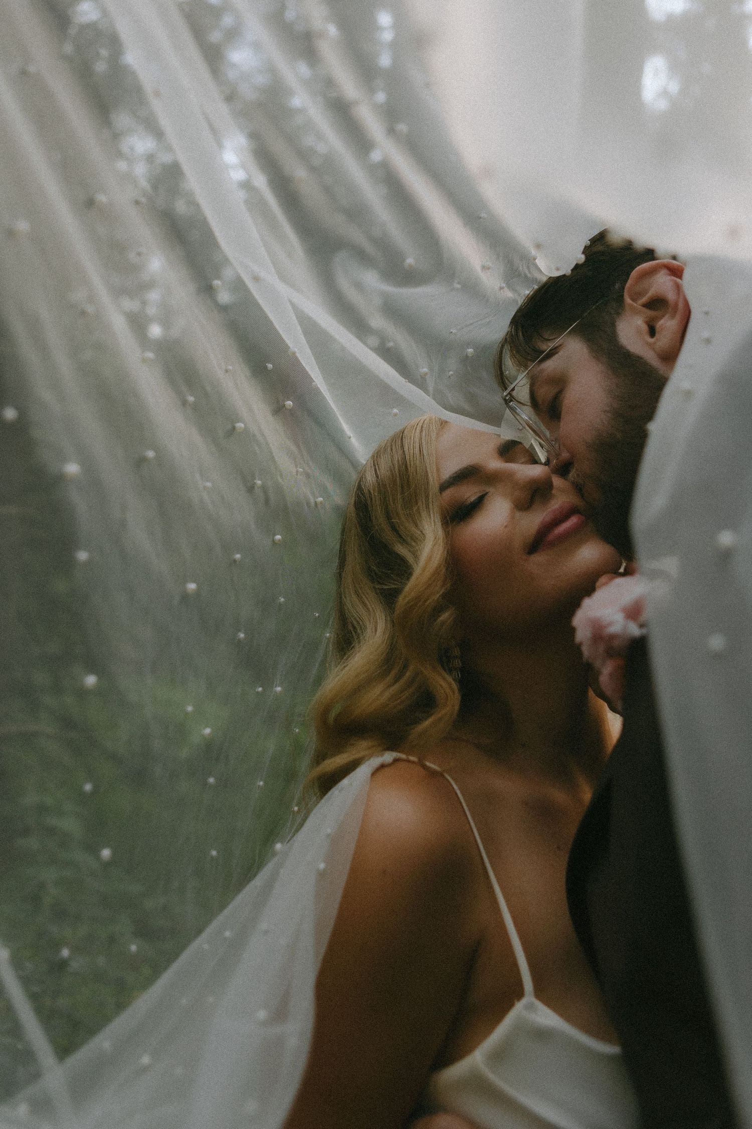 Romantic wedding portrait under a flowing veil with ethereal light filtering through.