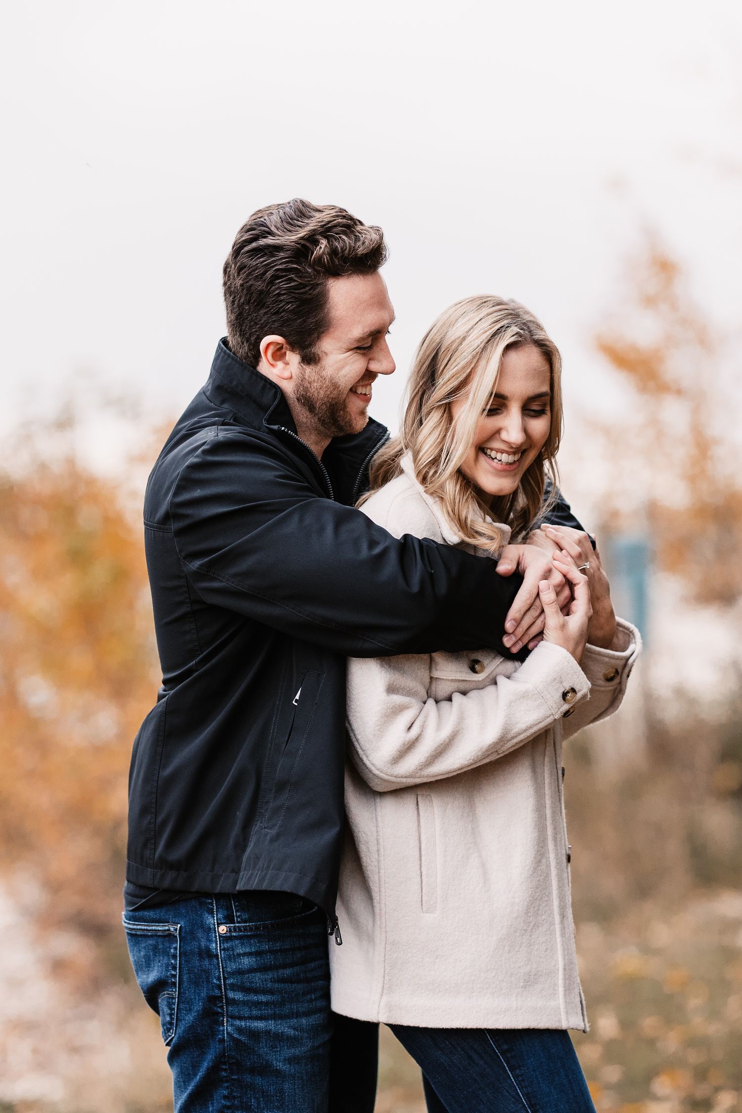 A joyful couple embraces while wearing cozy fall jackets against an autumn backdrop with warm colors.